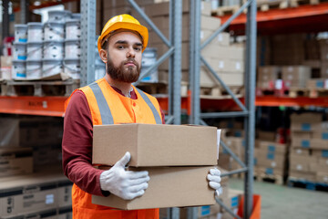 Gloved man in hardhat and workwear loading boxes with goods