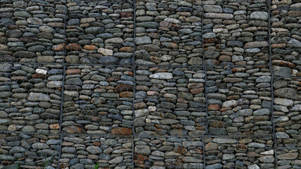 Gabion retaining wall - grey stones in gabion metallic baskets kept by retaining wall wire mesh. Backdrop design and eco wall and die-cut for artwork. Metallic basket net filled by stones as a fence.