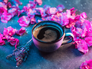 Ceramic cup of black espresso coffee on a neon background with purple bougainvillea flowers