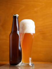 A tall glass of a pint of beer on a wooden table, a beer bottle. Unfiltered traditional wheat beer