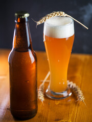 A tall glass of a pint of beer on a wooden table, a beer bottle. Unfiltered traditional wheat beer