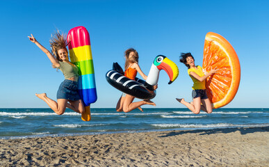 three happy girls on jumping motion with inflatable mattresses at the beach outdoors in summer...