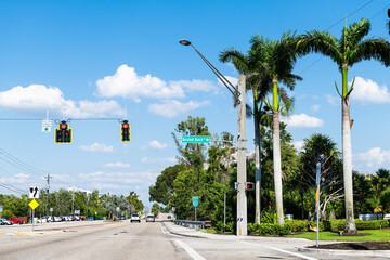 Palm trees on street road in Bonita Springs, Florida with sign for famous Barefoot Beach city town...