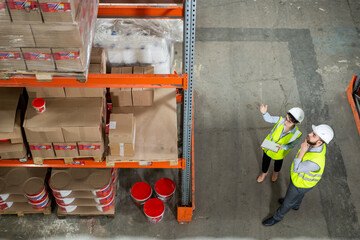 Two workes of warehouse in uniform having discussion in front of rack with packed goods