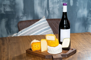 assorted cheese heads on a cutting board and a bottle of wine on a wooden table.