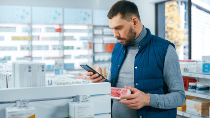 Fototapeta na wymiar Pharmacy Drugstore: Portrait of Handsome Young Caucasian Man Using Smartphone, Searching to Purchase Best Medicine, Drugs, Vitamins. Shelves full of Health Care, Wellness, Sports Supplements