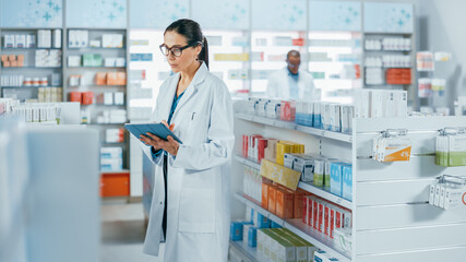 Pharmacy Drugstore: Beautiful Caucasian Pharmacist Uses Digital Tablet Computer, Checks Inventory of Medicine, Drugs, Vitamins, Health Care Products on a Shelf. Professional Pharmacist in Pharma Store