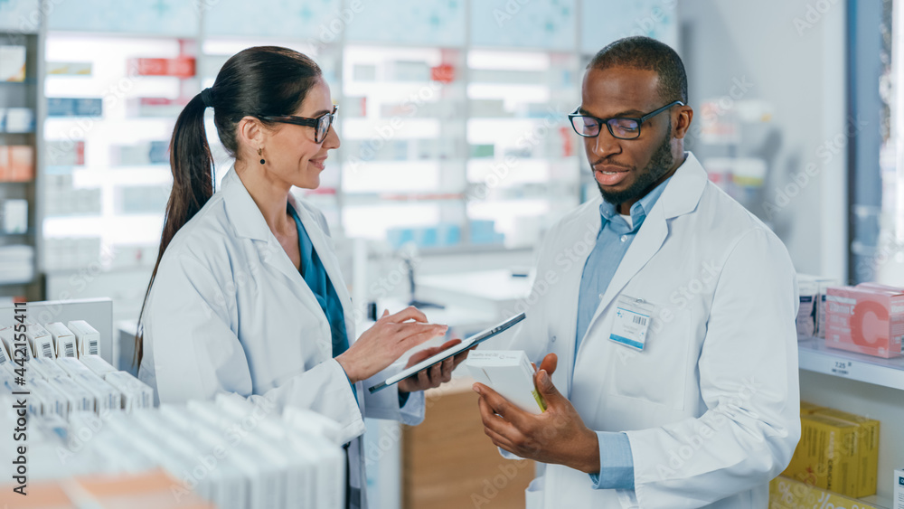 Wall mural pharmacy: black male and caucasian female pharmacists use digital tablet computer talk about medicin