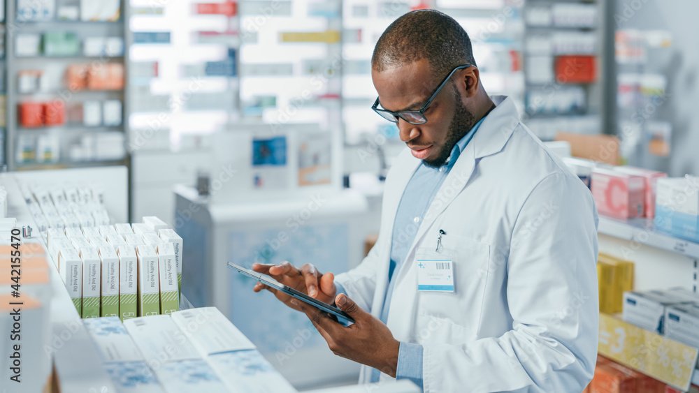 Wall mural Pharmacy: Portrait of Professional Black Pharmacist Uses Digital Tablet Computer, Checks Inventory of Medicine, Drugs, Vitamins, Health Care Products on a Shelf. Pharmacist in Drugstore Store