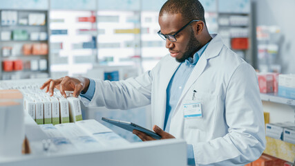 Pharmacy: Portrait of Professional Black Pharmacist Uses Digital Tablet Computer, Checks Inventory of Medicine, Drugs, Vitamins, Health Care Products on a Shelf. Pharmacist in Drugstore Store