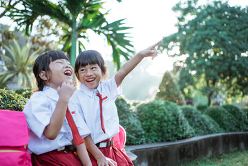 cute two asian student in uniform pointing away while sitting togehter in the park