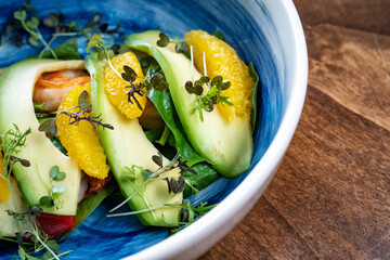 microgreen on avocado, shrimp and orange in blue plate.