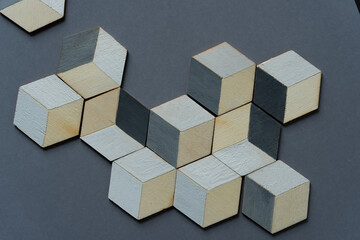 3d wooden cubes (hexagons) hand painted in white and various shades of gray acrylic paint, loosely arranged on a medium gray paper background, and photographed from above in a flat lay style with ambi