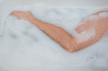 Funny picture of a man taking a relaxing bath. Close-up of male feet in a bubble bath. Top view