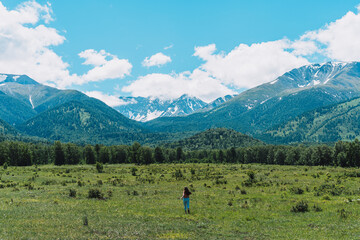 Fototapeta na wymiar Young girl runs on green meadows in front of the high mountains