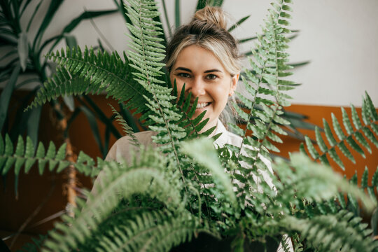 A young woman smiles and looks at camera, clutching pot of fern. Happy to engage in a hobby-to plant flowers