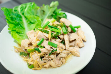 Stir-fried chicken with ginger and fresh vegetables salad in a white plate placed on a wooden board. Close-up