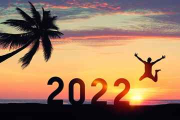 Silhouette man jumping with number like 2022 and palm tree at tropical beach on sunset sky abstract background. Happy new year and holiday celebration concept.