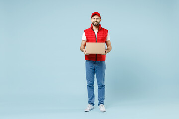 Full size body length delivery guy employee man in red cap white T-shirt vest uniform work as dealer courier hold blank cardboard box isolated on pastel blue color background studio. Service concept. - obrazy, fototapety, plakaty