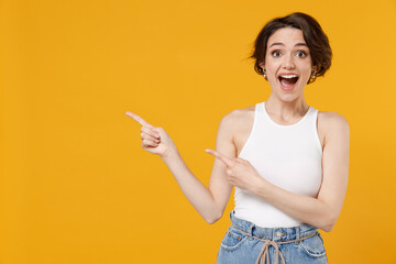 Young surprised amazed woman 20s with bob haircut wearing white tank top shirt point index finger...