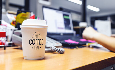 paper cup of coffee on table in office with soft-focus and over light in the background