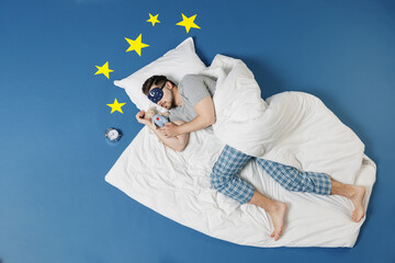 Full length top view young man in pajamas jam sleep mask relax at home lies wrap covered under...