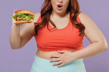 Close up cropped photo young chubby overweight plus size fit woman in red top warm up training hold fastfood burger put hand belly isolated on purple background gym Workout sport motivation concept.