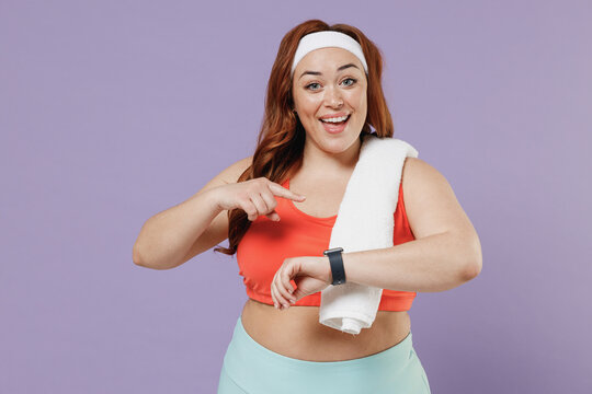 Young fun chubby overweight plus size big fat fit woman in red top towel warm up training point index finger on smart watch isolated on purple background home gym. Workout sport motivation concept