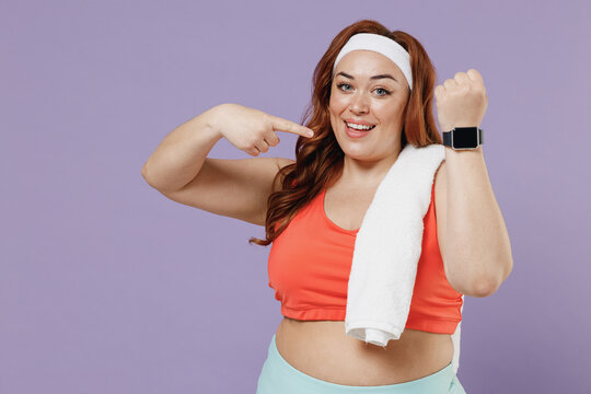 Young chubby overweight plus size big fat fit woman in red top towel warm up training point finger on smart watch blank screen isolated on purple background home gym Workout sport motivation concept - Powered by Adobe