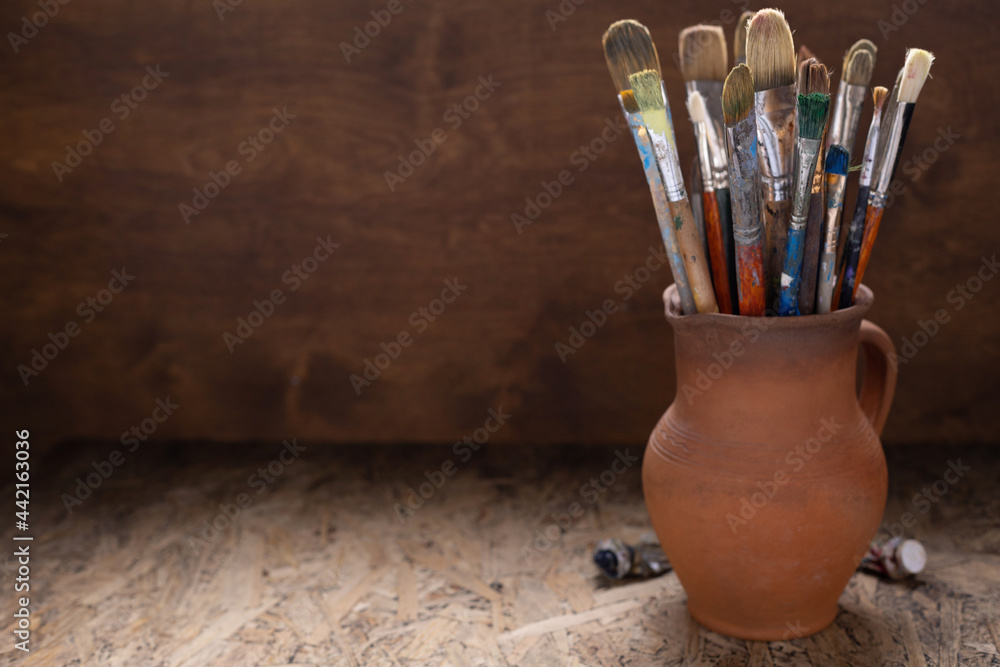 Poster Paint brush in clay jug and used tubes on wooden table background . Paintbrush for art painting