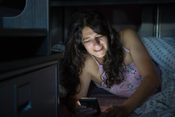 Happy woman reading at night. Mobile light on the face. Gloom