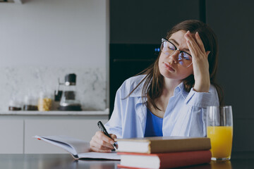Smart tired sleepy young housewife woman 20s in blue shirt casual clothes glasses writing down...