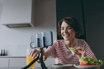 Fototapeta na wymiar Bottom view young smiling housewife woman in casual clothes t-shirt eat breakfast lunch use mobile cell phone count calories cook food in light kitchen at home alone Healthy diet lifestyle concept