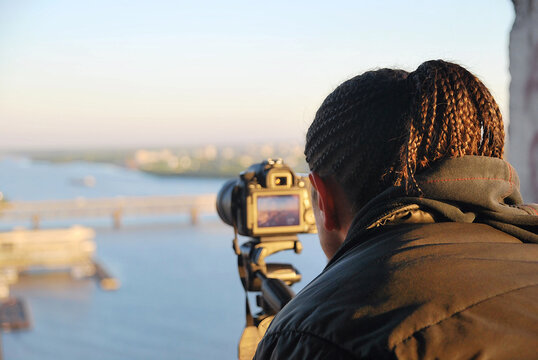 Photographer in dreadlocks with a camera on the roof is taking pictures of the cityscape, close-up.