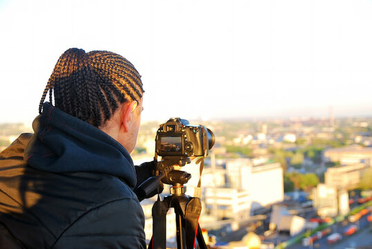 Photographer in dreadlocks with a camera on the roof is taking pictures of the cityscape, close-up.
