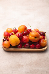 Wooden tray with fresh cherries, plums and apricots