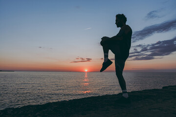 Silhouette side view full size young strong sporty athletic toned fit sportsman man in sports clothes warm up training at sunrise sun dawn over sea beach outdoor on pier seaside in summer day morning