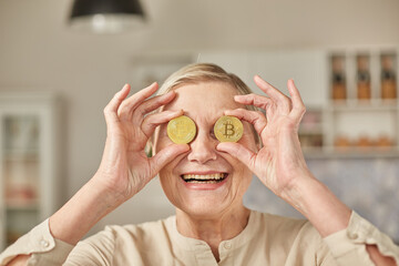 An elderly woman holds bitcoin coins in her hands near her eyes. Seniors retirement happy life...