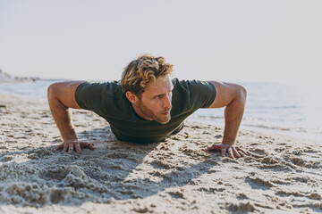 Full size front view young sporty athletic toned fit sportsman man 20s wearing sports clothes warm up training in push up position at sunrise sun over sea beach outdoor seaside in summer day morning.