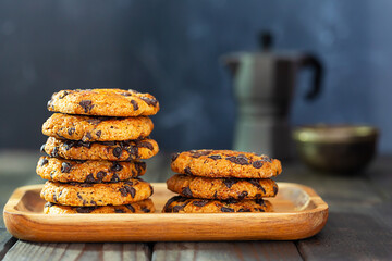 Cookies with chocolate pieces laid on a wooden plate and a coffee pot