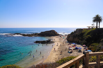 people relaxing on the sandy beach with colorful umbrellas with vast blue ocean water and lush green hillsides with palm trees at Treasure Island Beach in Laguna Beach California  © Marcus Jones