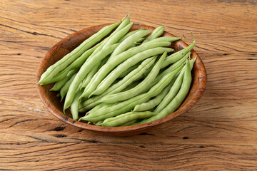 A group of green bean pods in a bowl over wooden table