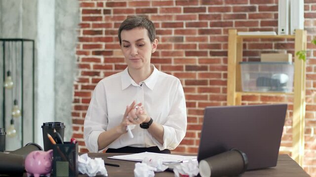 Disgruntled woman writes with a pen on sheet, crosses out the written and aggressively rumpling paper throws a crumpled sheet on the desktop in office.