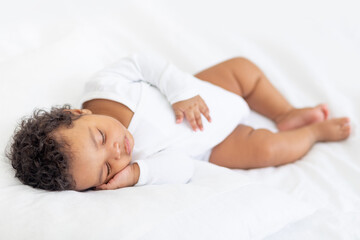 African-American little baby sleeps on a white bed at home with her hand folded under her cheek