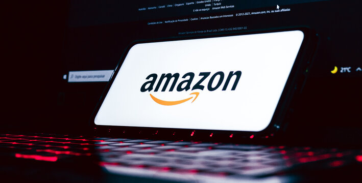 Amazon. A logo da Amazon na tela de um celular que est&aacute; sobre um teclado de notebook com ilumina&ccedil;&atilde;o de leds. Fotografia em ambiente noturno. Site, Com&eacute;rcio eletr&ocirc;nico, online, Venda, Varejo, produto.
