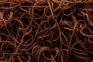The texture of the background of woolen or nylon threads for knitting resembling a brown rope, shot close-up on the theme of hobbies and hand-made in dark colors