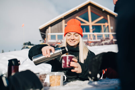 Leende kvinna h&auml;ller upp kaffe ut termos utomhus