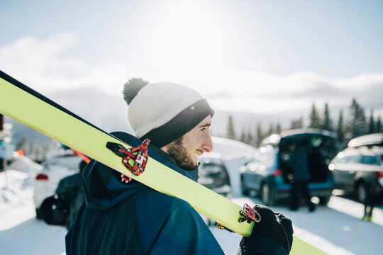 Leende man g&aring;r med skidor p&aring; axeln under solig vinterdag