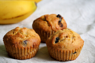 three vegan gluten-free banana muffins stand on a beige background next to yellow bananas, side view. homemade diet lactose free, egg free, gluten free