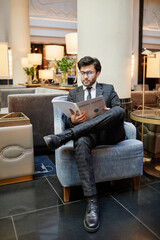 Vertical full length portrait of successful Middle-Eastern businessman reading documents while...